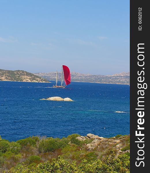 Red sails yacht sailing in the beautiful blue windy sea off the Sardinian coast near Palau, Italy, with wind in its sails