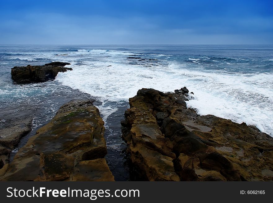 A split rock with waves of white sea foam swirling around them. A split rock with waves of white sea foam swirling around them