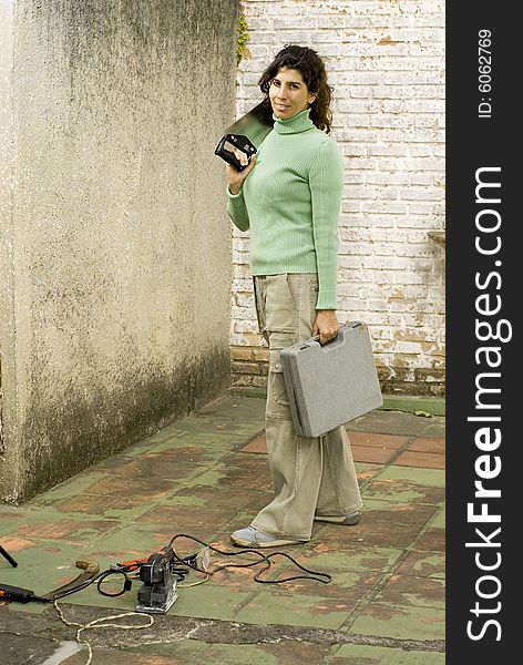 Woman stands in unfinished room holding hand saw and a toolkit. She is looking at the camera. Vertically framed photo. Woman stands in unfinished room holding hand saw and a toolkit. She is looking at the camera. Vertically framed photo.