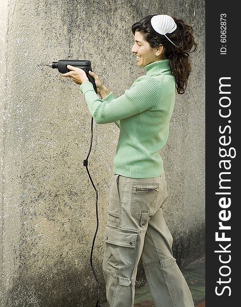 Woman with mask on head drills hole into wall with electric drill. Vertically framed photo. Woman with mask on head drills hole into wall with electric drill. Vertically framed photo.