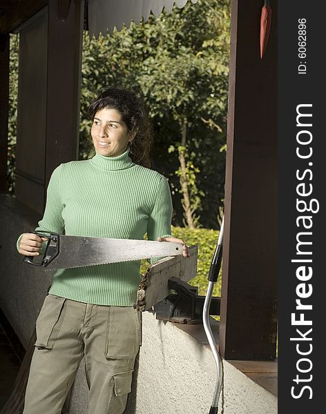 Woman stands facing the camera holding a handsaw. She is looking to the side. Vertically framed photo. Woman stands facing the camera holding a handsaw. She is looking to the side. Vertically framed photo.