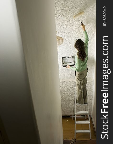 Woman stands on ladder and paints wall with paint roller. Vertically framed photo. Woman stands on ladder and paints wall with paint roller. Vertically framed photo.
