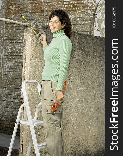 Smiling woman holding a saw and standing on a ladder. Vertically framed photo. Smiling woman holding a saw and standing on a ladder. Vertically framed photo.