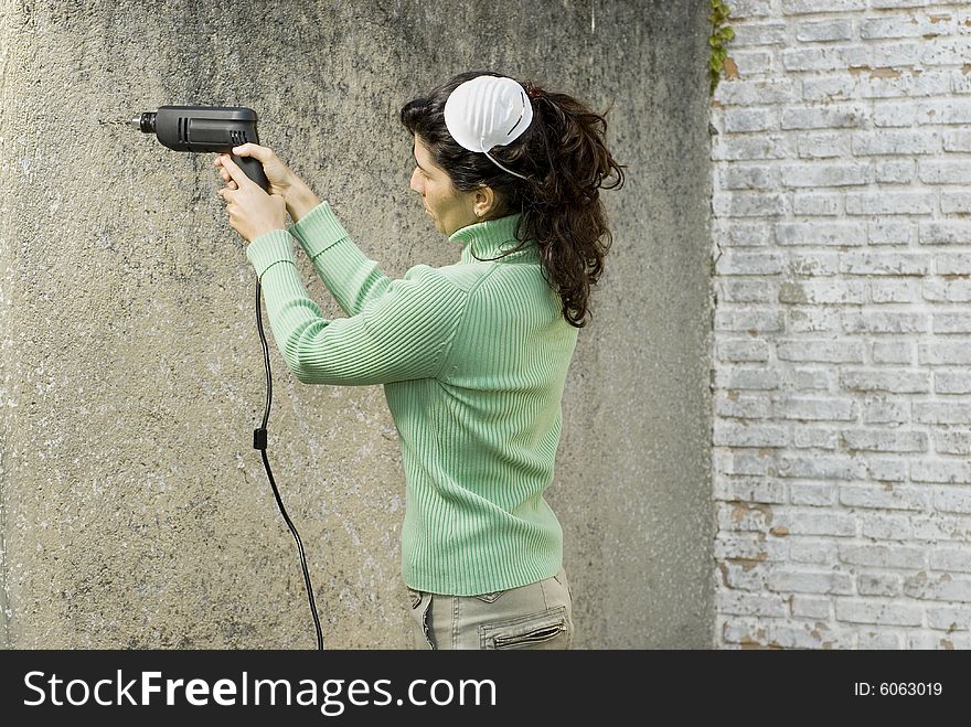 Woman with mask on head drills hole into wall with electric drill. Horizontally framed photo. Woman with mask on head drills hole into wall with electric drill. Horizontally framed photo.