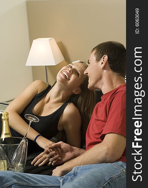 Man and woman relax on bed. A bucket of champagne is between them and they are holding hands and laugh. Horizontally framed photo. Man and woman relax on bed. A bucket of champagne is between them and they are holding hands and laugh. Horizontally framed photo.