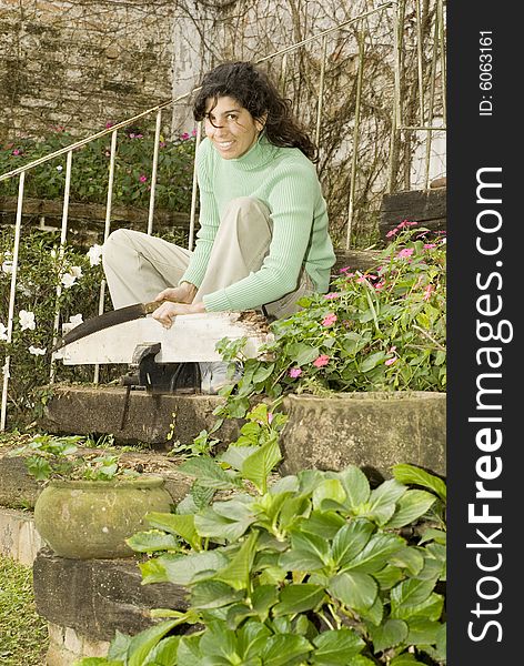 Smiling woman cuts board in vice. Woman is sitting on stairs in garden. Vertically framed photo. Smiling woman cuts board in vice. Woman is sitting on stairs in garden. Vertically framed photo.