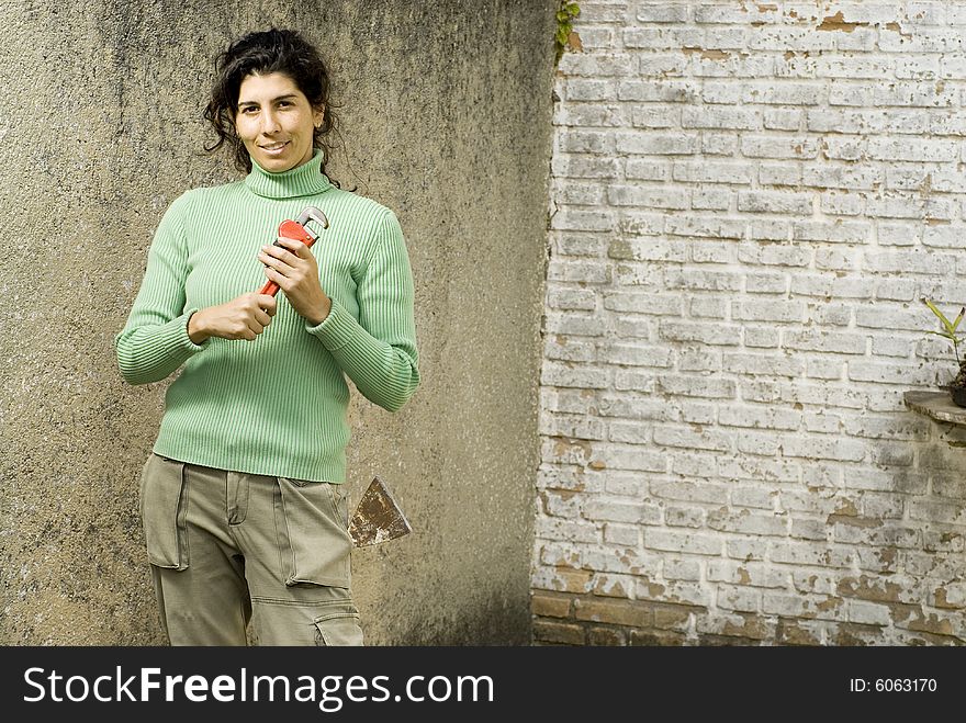 Smiling woman holding a wrench standing next to a wall. Horizontally framed photo. Smiling woman holding a wrench standing next to a wall. Horizontally framed photo.