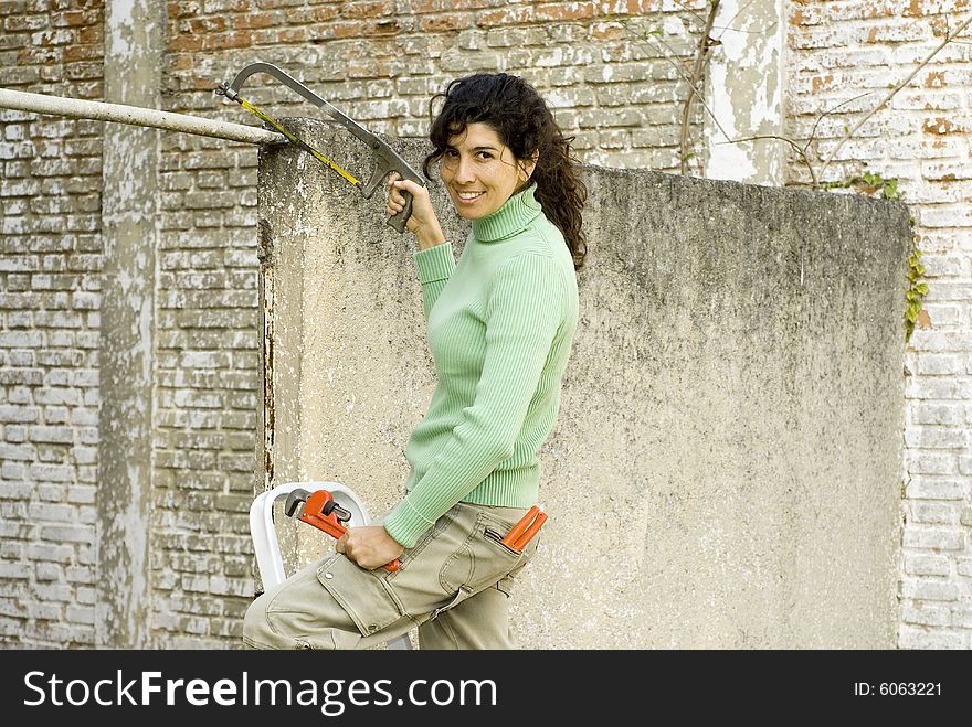 Smiling woman standing on a stool holding a wrench and a saw. Horizontally framed photo. Smiling woman standing on a stool holding a wrench and a saw. Horizontally framed photo.