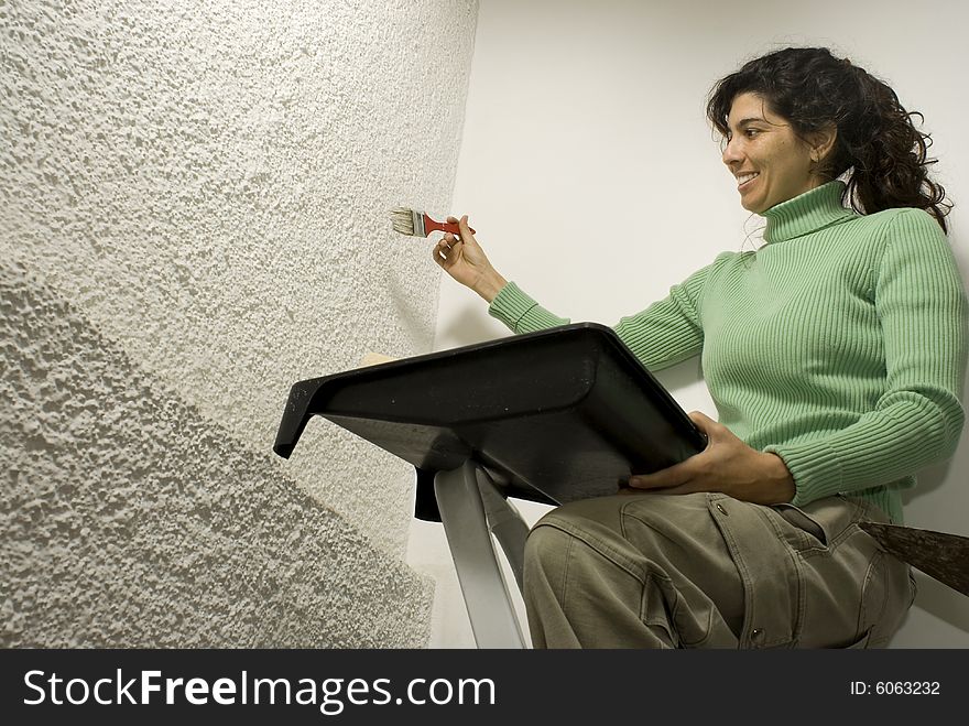 A smiling woman holding a paint tray paints a wall using a brush. Horizontally framed photo. A smiling woman holding a paint tray paints a wall using a brush. Horizontally framed photo.