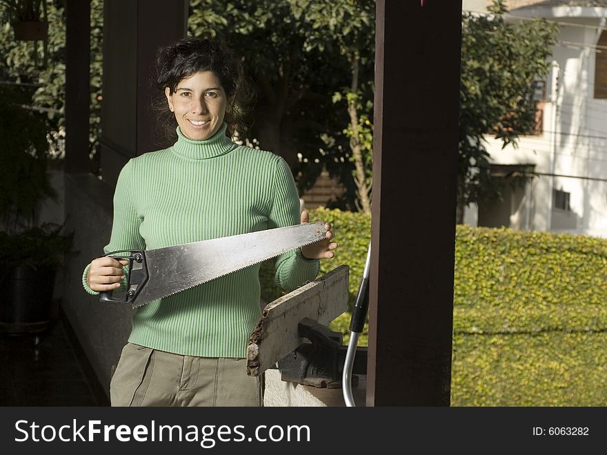 Woman stands facing the camera holding a handsaw. She is looking to the side. Horizontally framed photo. Woman stands facing the camera holding a handsaw. She is looking to the side. Horizontally framed photo