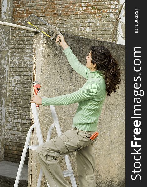 Woman holding a saw and standing on a ladder. Vertically framed photo. Woman holding a saw and standing on a ladder. Vertically framed photo.