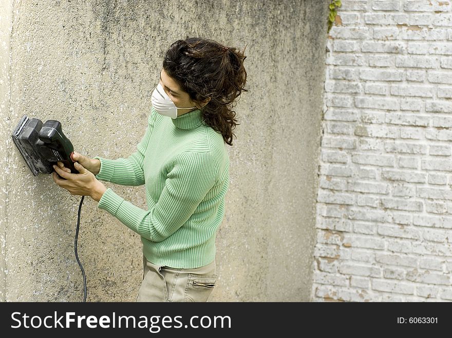Woman wearing a painter's mask using a sander on a wall. Horizontally framed photo. Woman wearing a painter's mask using a sander on a wall. Horizontally framed photo.