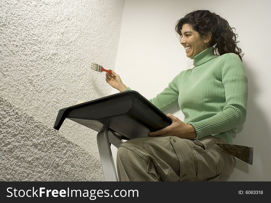 Smiling woman holding a paint tray and painting a wall with a brush. Horizontally framed photo. Smiling woman holding a paint tray and painting a wall with a brush. Horizontally framed photo.