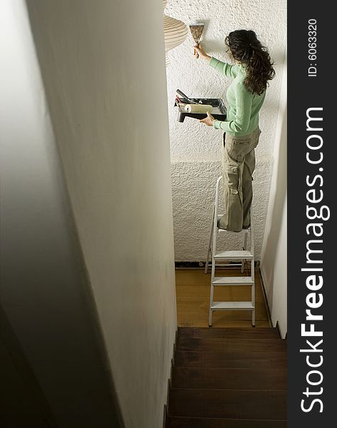 Woman stands on ladder and paints wall with paint roller. Vertically framed photo. Woman stands on ladder and paints wall with paint roller. Vertically framed photo.