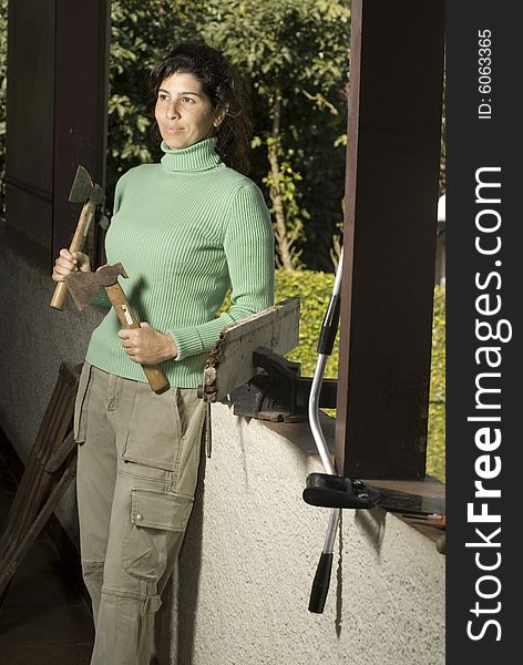 Smiling woman leans against a wall holding two hatchets. Vertically framed photo. Smiling woman leans against a wall holding two hatchets. Vertically framed photo.