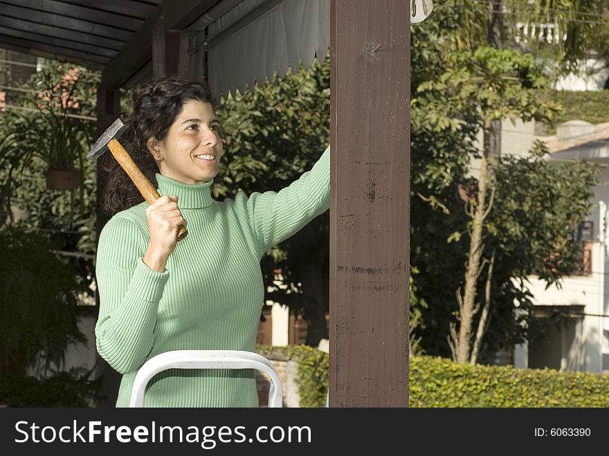 Smiling woman hammers nail into post. She is holding a hammer. Horizontally framed photo. Smiling woman hammers nail into post. She is holding a hammer. Horizontally framed photo.