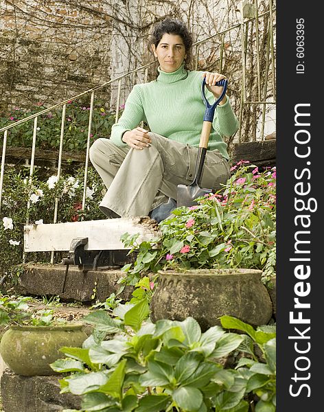 Woman holding short shovel sits on stairs in garden. She is looking at the camera. Vertically framed photo. Woman holding short shovel sits on stairs in garden. She is looking at the camera. Vertically framed photo.