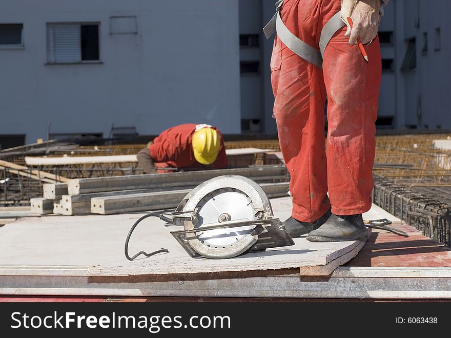 Construction worker's legs are shown standing next to rotary saw. Horizontally framed photo. Construction worker's legs are shown standing next to rotary saw. Horizontally framed photo.