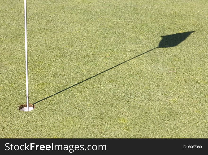 Hole and shadow of a golf green flag on the green