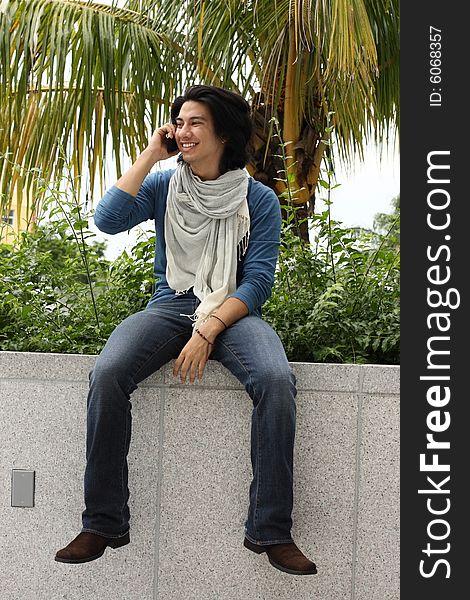 Young male sitting on a ledge talking on the phone. Young male sitting on a ledge talking on the phone.