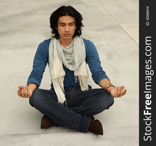 Young male meditating with concrete ground background. Young male meditating with concrete ground background.