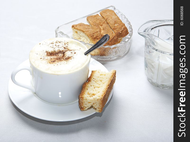 Coffee in white cup with spoon and caramal rusk, more rusks and milk in background. Coffee in white cup with spoon and caramal rusk, more rusks and milk in background