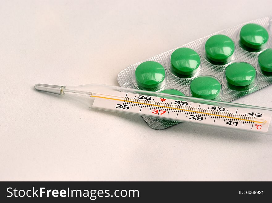 The medical thermometer and green tablets on a light grey background. The medical thermometer and green tablets on a light grey background