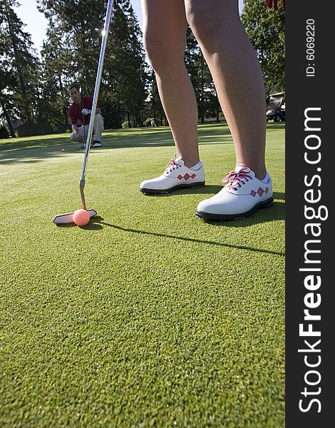 A woman is standing on the green of a golf course.  She is about to putt the ball into the hole.  Vertically framed shot. A woman is standing on the green of a golf course.  She is about to putt the ball into the hole.  Vertically framed shot.