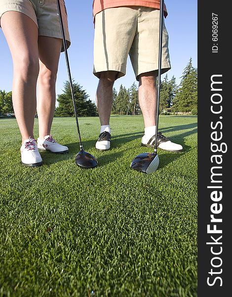A man and a woman are standing on a golf course.  You can only see their legs and their clubs.  Vertically framed shot. A man and a woman are standing on a golf course.  You can only see their legs and their clubs.  Vertically framed shot.
