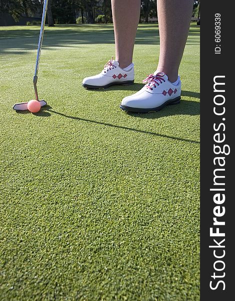 A woman is standing on the green of a golf course.  She is about to putt the ball into the hole.  Vertically framed shot. A woman is standing on the green of a golf course.  She is about to putt the ball into the hole.  Vertically framed shot.