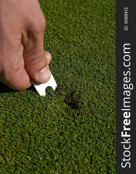 Man's hand repairs divot on golf green. Vertically framed photo. Man's hand repairs divot on golf green. Vertically framed photo.