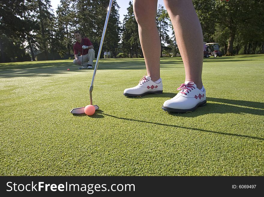 A woman is standing on the green of a golf course.  She is about to putt the ball into the hole.  Horizontally framed shot. A woman is standing on the green of a golf course.  She is about to putt the ball into the hole.  Horizontally framed shot.