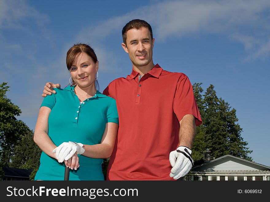 Golfers stand in front of camera. Man has arm around woman and they are smiling at camera. Horizontally framed photo. Golfers stand in front of camera. Man has arm around woman and they are smiling at camera. Horizontally framed photo.