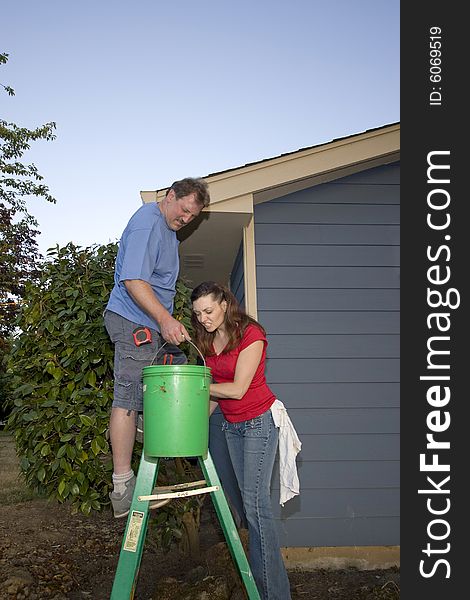 Man and woman standing on a ladder near a blue house. Vertically framed shot. Man and woman standing on a ladder near a blue house. Vertically framed shot.