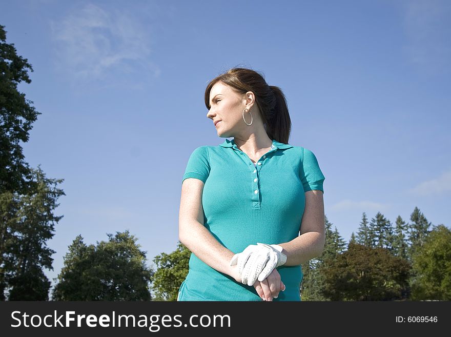 A young woman is standing on a golf course holding a club.  She is looking away from the camera.  Horizontally framed shot. A young woman is standing on a golf course holding a club.  She is looking away from the camera.  Horizontally framed shot.