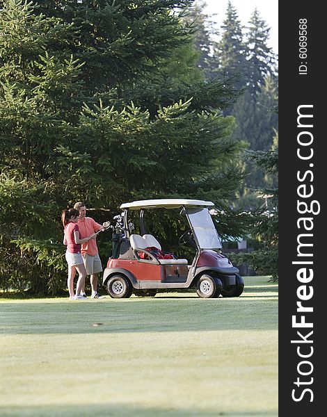A happy couple standing near their golf cart inspect their golf clubs. Vertically framed photo. A happy couple standing near their golf cart inspect their golf clubs. Vertically framed photo