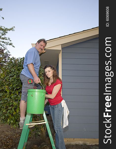 Man and woman standing on a ladder near a blue house. Vertically framed shot. Man and woman standing on a ladder near a blue house. Vertically framed shot.