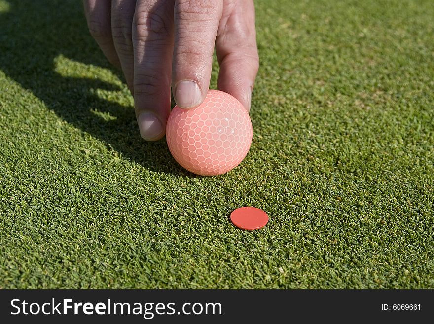A man is holding a golf ball and is about to set it on a marker. Horizontally framed shot. A man is holding a golf ball and is about to set it on a marker. Horizontally framed shot.