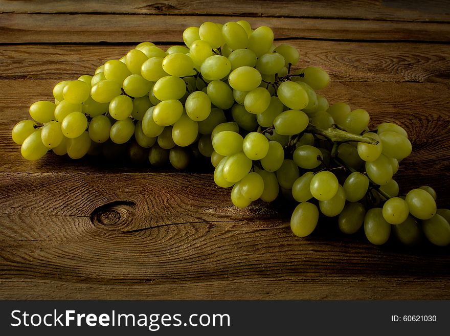 Bunch of green grapes on a dark wooden background. Selective focus. The toning. Bunch of green grapes on a dark wooden background. Selective focus. The toning