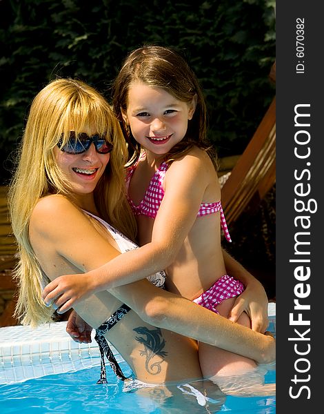 Young blond girl and her sister enjoying the sun in and around the swimming pool. Young blond girl and her sister enjoying the sun in and around the swimming pool