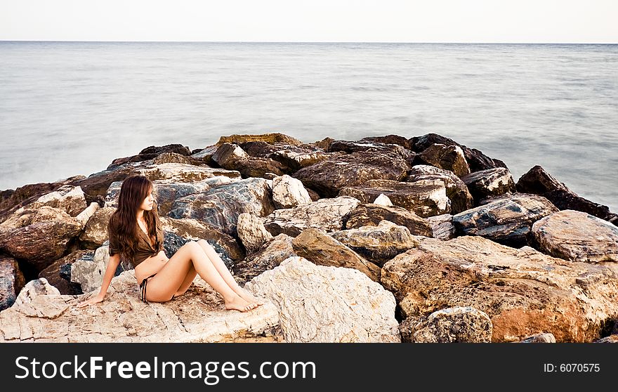 Young woman in rocks surrounded by long exposed sea.