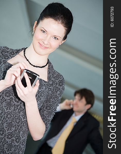 A charming girl holding a cell phone and a man speaking on the phone at the background. A charming girl holding a cell phone and a man speaking on the phone at the background