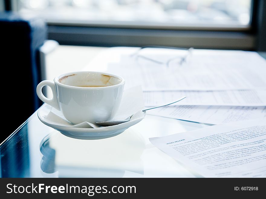 A cup of coffee, eyeglasses and papers lying on the table. A cup of coffee, eyeglasses and papers lying on the table