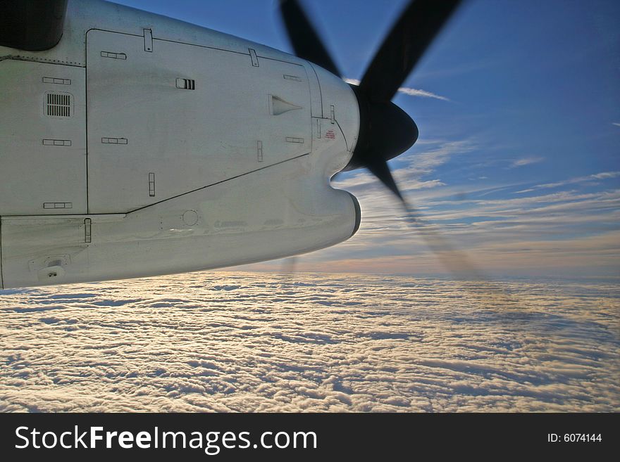 Sunrise appearing above the clouds seen under the engine cowling and propeller of a turboprop aircraft. Sunrise appearing above the clouds seen under the engine cowling and propeller of a turboprop aircraft.