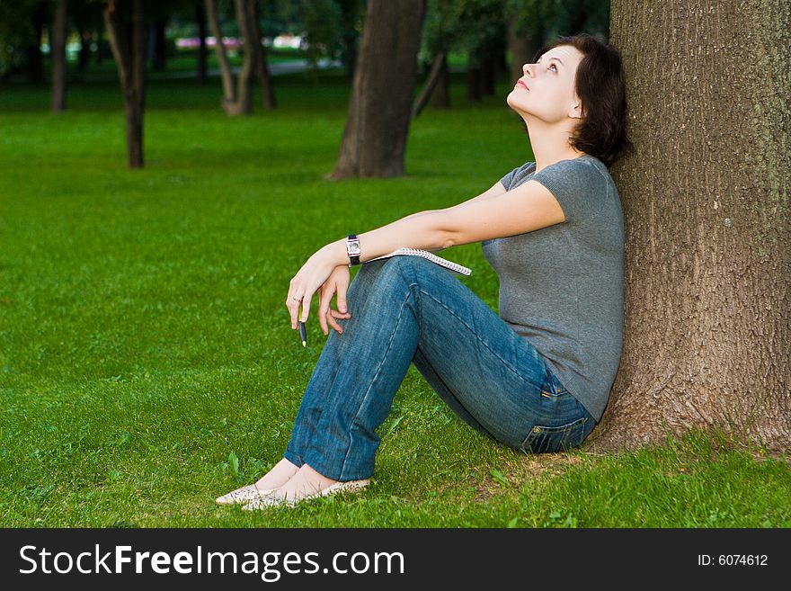 Girl sits under a tree with a thoughtful kind