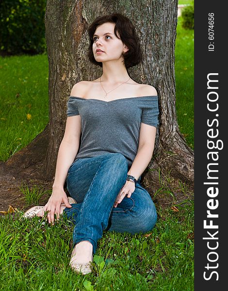Beautiful girl has a rest sitting on a grass under a tree. Beautiful girl has a rest sitting on a grass under a tree