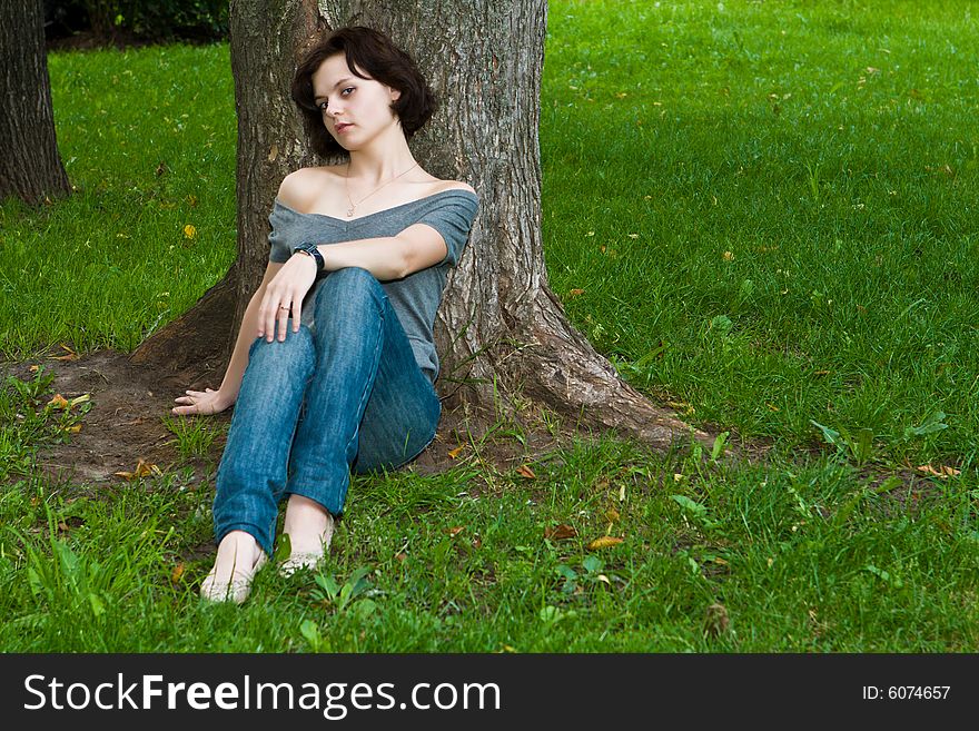 Beautiful girl has a rest sitting on a grass under a tree. Beautiful girl has a rest sitting on a grass under a tree