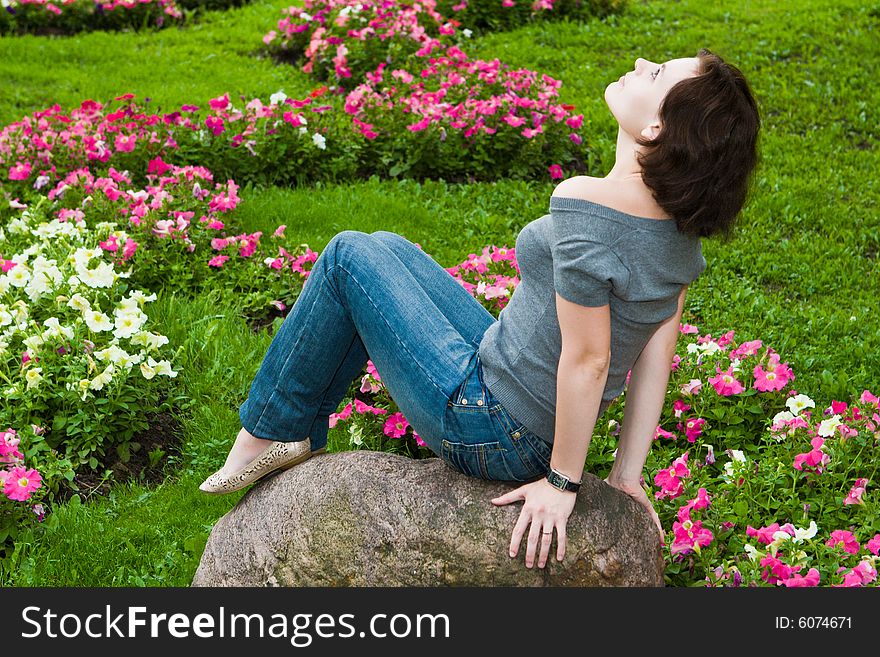 Girl sits on a stone on a background of a lawn with colors