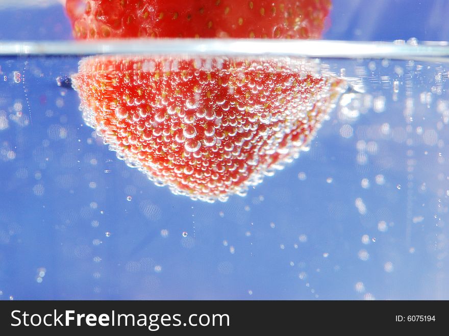 A fresh strawberry being submerged in water with bubbles. A fresh strawberry being submerged in water with bubbles.