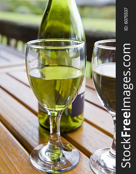 Glasses of white wine on a wooden table at an outside restaurant on a cloudy day in the countryside. Glasses of white wine on a wooden table at an outside restaurant on a cloudy day in the countryside.